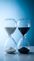 Two glass hourglasses with white and black sand on blue background, symbolizing time passing, deadline, and contrast concepts.