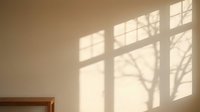 Warm sunlight streaming through window creates dramatic tree branch shadows on neutral beige wall in minimalist interior space for home decor concepts.