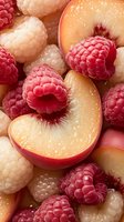 Fresh peach slices and raspberries with water droplets creating colorful summer fruit mix for healthy eating and culinary backgrounds.