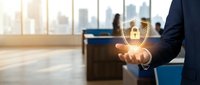 Young professional man in business suit holding glowing padlock symbol in palm, representing cybersecurity, data protection, and digital safety in modern office environment with city skyline.