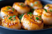 Pan seared sea scallops with golden brown crust garnished with fresh herbs and butter sauce, close up view of gourmet seafood appetizer on dark plate.