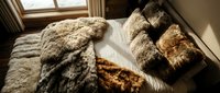 Cozy bedroom interior with unmade bed, fluffy textured blankets and pillows in warm sunlight streaming through window creating peaceful morning atmosphere.