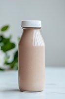 Fresh chocolate milk or protein shake in glass bottle with white cap on light background, green leaves bokeh, healthy lifestyle concept for food blogs.