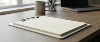 Minimalist workspace with blank clipboard and lined paper on wooden desk near window. Clean office setup for business planning and note-taking.