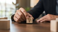 Male hand placing wooden block with lightbulb icon on table, representing innovation, business strategy, and creative problem-solving for corporate environments.