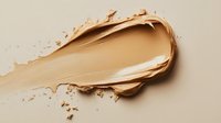 Creamy foundation smear showing smooth texture and light beige tone against neutral background, demonstrating makeup product consistency and coverage.