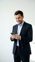 Happy businessman in dark suit using smartphone, smiling while texting or browsing mobile device on white background for business communication concepts.