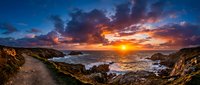 Dramatic coastal sunset with golden and orange sky reflecting on rocky shoreline and ocean waves during dusk, suitable for travel and nature backgrounds.