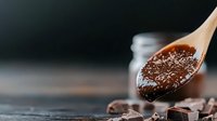 Wooden spoon filled with cocoa powder over dark chocolate pieces on rustic surface for baking and confectionery preparation.
