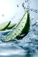 Fresh aloe vera slice splashing in clear water with dynamic motion and droplets, showcasing natural skincare ingredient on light blue background.