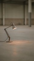 Vintage industrial desk lamp with articulated arm casting warm light in empty warehouse space, suitable for design and creative projects.