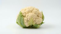 Fresh whole cauliflower head with green leaves isolated on white background, suitable for food, nutrition, cooking, and healthy eating content.