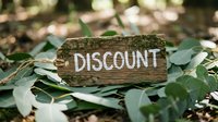 Rustic wooden tag with discount text resting on green leaves outdoors, evoking natural eco-friendly sale and shopping promotion concepts.