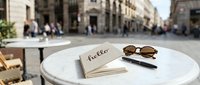Notebook with hello inscription, sunglasses and pen on marble table at outdoor European cafe with blurred city street background.