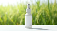 White frosted glass dropper bottle with pipette on clean surface against blurred green natural background for skincare serum cosmetic product mockup.