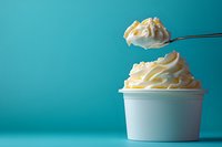 Creamy soft serve vanilla ice cream swirled in white paper cup with spoonful floating above against turquoise background, minimalist summer dessert composition.