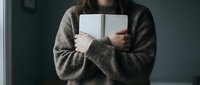 Young woman in cozy knit sweater holding open notebook journal for writing reading studying creative work lifestyle concept indoor natural lighting.