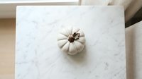 White decorative pumpkin on marble surface for autumn home decor, seasonal styling, and fall interior design projects.
