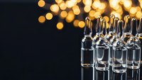 Medical glass vials arranged in rows with warm golden bokeh lights creating elegant pharmaceutical laboratory atmosphere for healthcare design.