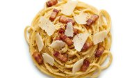 Creamy pasta carbonara with crispy bacon, parmesan cheese shavings, and fresh cracked pepper on white background. Perfect for food blogs, recipes, menus.