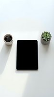 Minimalist workspace with black tablet, coffee cup and succulent plant on clean white desk surface for modern office productivity and remote work setup.
