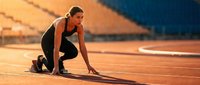 Athletic woman in starting position on running track during golden hour sunset preparing for sprint race at stadium.