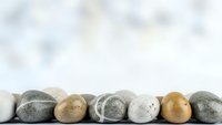 Smooth river stones arranged in row on white surface against soft blurred background for spa wellness meditation zen balance natural decoration concepts.