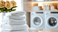 Fresh white folded towels stacked in laundry room with washing machines and hydrangea flowers, creating clean and organized home atmosphere for lifestyle blogs.