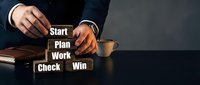 Businessman arranging wooden blocks with words Start, Plan, Work, Check, Win on dark desk, symbolizing strategic business planning and success.