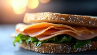 Fresh turkey sandwich with lettuce on toasted whole grain bread, close-up view with soft bokeh background lighting, appetizing deli meal preparation.