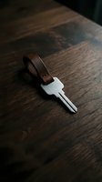 Silver key with brown leather keychain loop resting on dark wooden surface, suitable for security, access, and home ownership concepts.