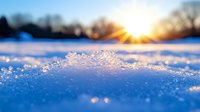 Macro shot of crystalline snow surface glowing in golden sunset light with bokeh effect and sun rays creating magical winter atmosphere in nature landscape.