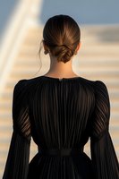 Back view of young woman in elegant black pleated dress with classic low bun hairstyle against soft blurred background during golden hour lighting.