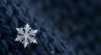 Single delicate snowflake with intricate crystalline structure resting on dark blue winter fabric surface creating seasonal holiday atmosphere.