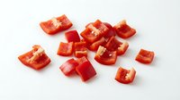 Fresh red bell pepper pieces chopped and diced on white background, ready for cooking and meal preparation in kitchen recipes.