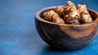 Fresh raw Jerusalem artichokes in wooden bowl on blue background. Natural organic sunchokes for healthy cooking and seasonal recipes.