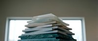 Stack of various books piled high against bright window light creating silhouette effect for education and learning concepts in library or study space.