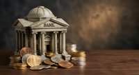 Classical bank building model with stacked coins on wooden surface representing financial services, savings, investment and economic growth concepts.
