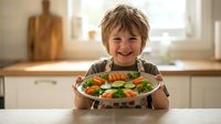 Happy young boy holding fresh vegetable salad plate in bright kitchen, promoting healthy eating habits and nutritious meals for children.