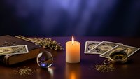 Mystical fortune telling setup with tarot cards, crystal ball, burning candle and dried herbs on wooden table creating atmospheric divination scene.