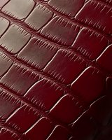 Burgundy crocodile leather texture with embossed pattern showing detailed scales and natural grain surface in dark red color, suitable for luxury fashion backgrounds.