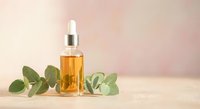 Golden serum bottle with dropper surrounded by fresh eucalyptus leaves on neutral background for skincare and wellness products.