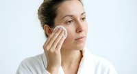 Young Caucasian woman applying skincare product with cotton pad on face during daily beauty routine. Natural makeup removal and facial cleansing concept.