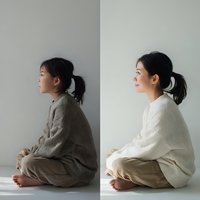 Young Asian woman in meditation pose wearing neutral sweater sitting cross-legged in minimalist studio setting for wellness and mindfulness concepts.