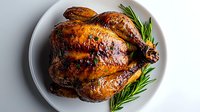 Whole roasted chicken with crispy golden-brown skin and fresh rosemary garnish served on white plate, shot from above showing juicy glaze and caramelized surface.