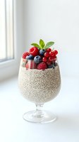 Chia seed pudding topped with fresh berries and mint in glass cup on white background for healthy breakfast and superfood recipes.