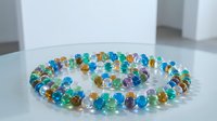 Colorful glass beads arranged in circular pattern on white surface, featuring vibrant blue, green, amber, and purple tones for jewelry design and craft projects.