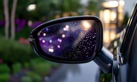 Car side mirror reflecting evening bokeh lights and raindrops creating magical starry effect against dark background, selective focus on mirror surface.