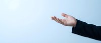 Caucasian male hand in dark business suit sleeve gesturing open palm against light blue background, conveying welcome, offer, or presentation concept for corporate communications.