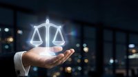 Lawyer holding glowing scales of justice symbol in palm against blurred city skyline at night, representing legal services, law firm, attorney consultation, compliance, and fairness.